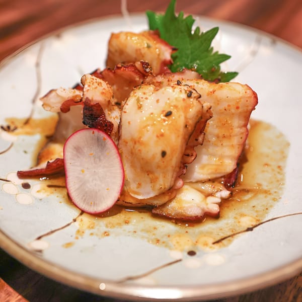 MF Sushi's grilled octopus with a radish slice and green garnish on a decorative plate.