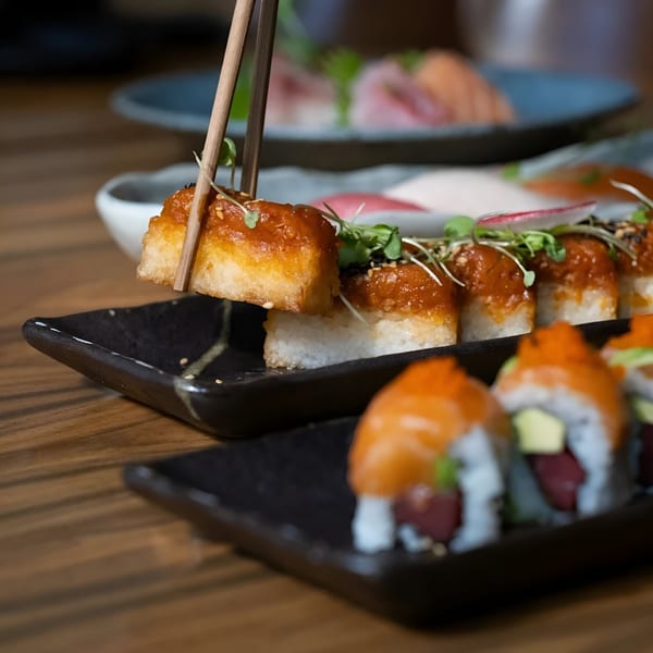 Chopsticks holding a piece of MF Sushi's crispy rice with spicy tuna, garnished with microgreens.