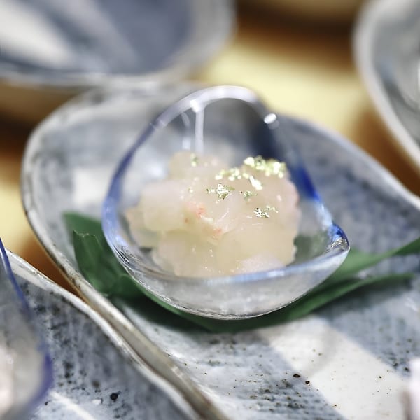 MF Sushi's delicate white seafood dish with gold flakes, served in a small glass bowl on a patterned plate.