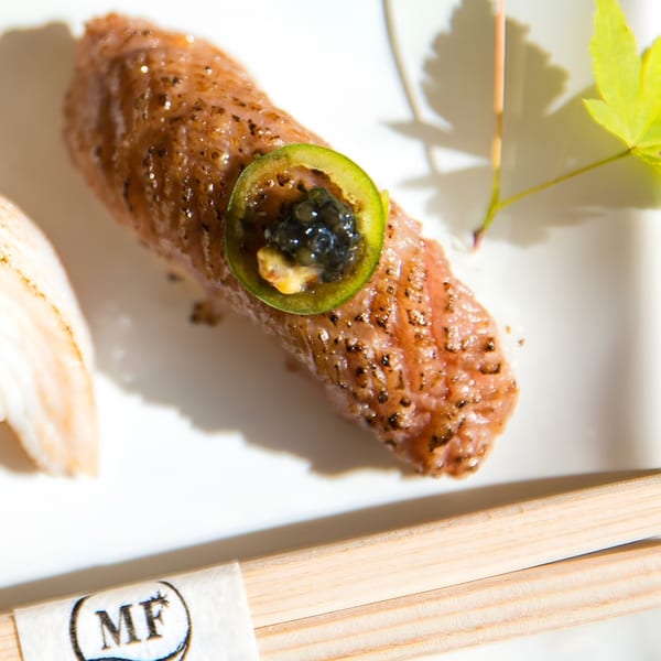 MF Sushi's seared nigiri with a slice of jalapeño and black caviar, alongside chopsticks.