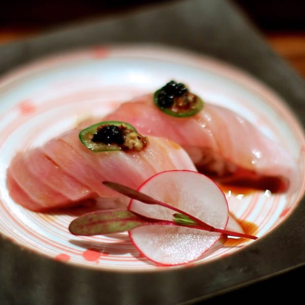Two MF Sushi nigiri pieces with fish, jalapeño, and caviar, garnished with radish slices.