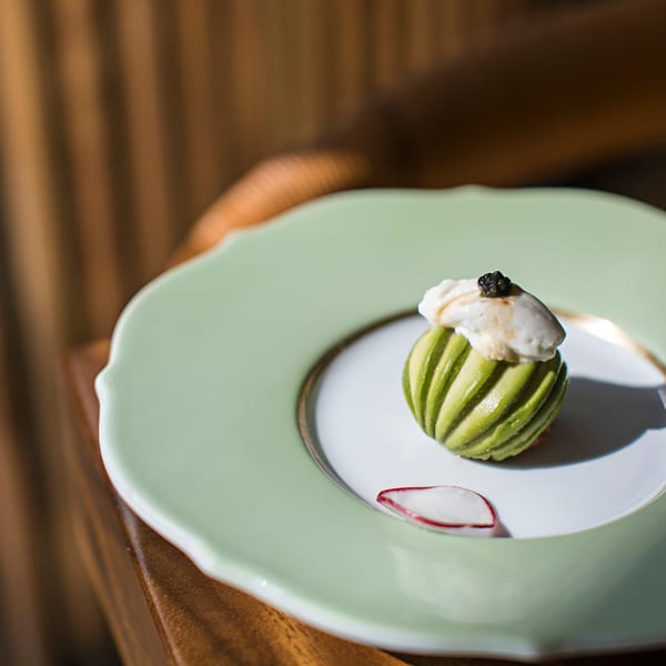 MF Sushi's green striped avocado dish topped with white cream and black caviar, on a light green plate.