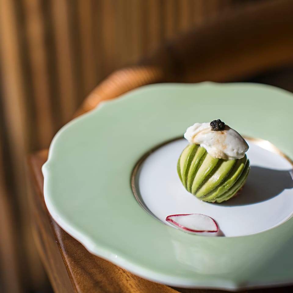 MF Sushi's green striped avocado dish topped with white cream and black caviar, on a light green plate.