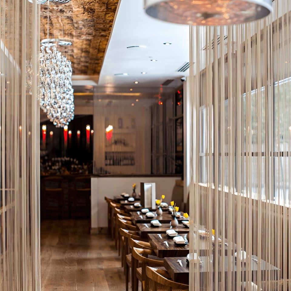 MF Sushi dining room with long wooden tables set with white napkins and yellow flowers, divided by string curtains.